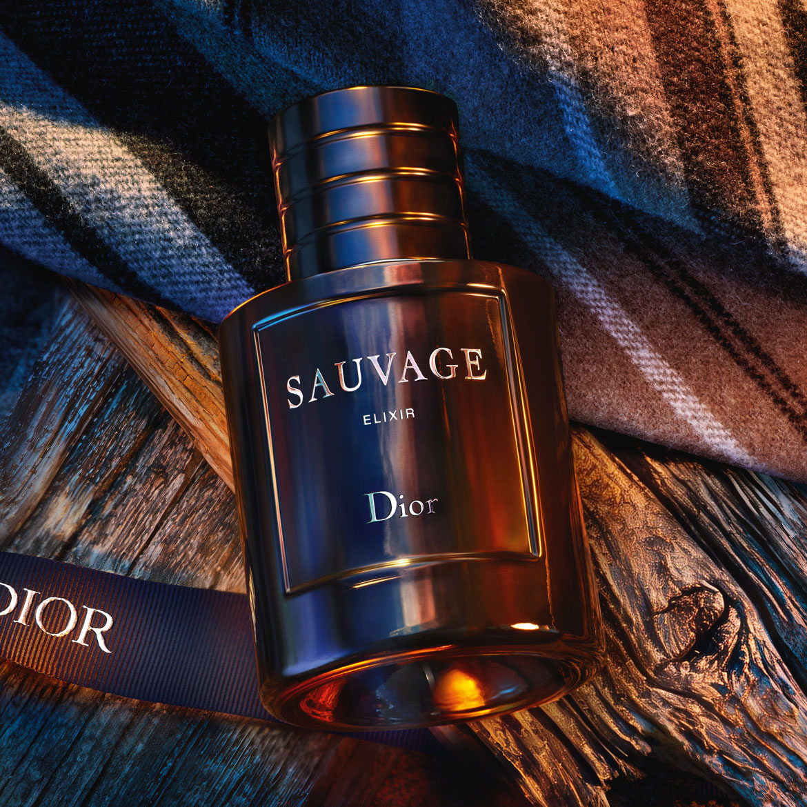 „Sauvage Elixir“ aromatas tamsiame stikliniame buteliuke su „Dior“ logotipu, padėtas ant medinės lentos ir languoto audinio, spinduliuoja prabangą ir šilumą.