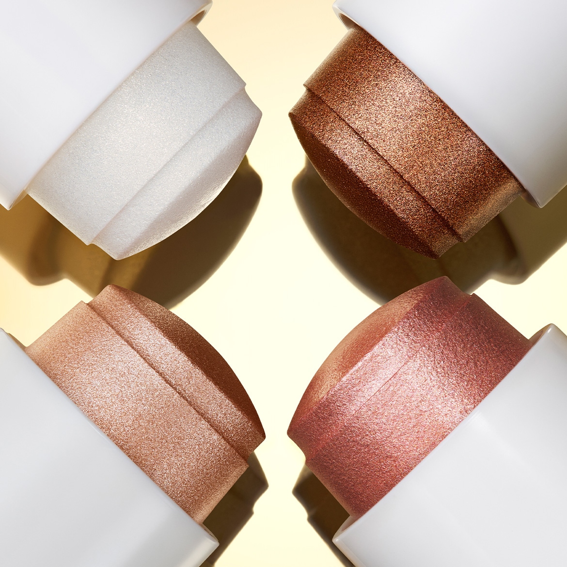 Keturių skirtingų atspalvių kreminiai kontūravimo pieštukai su baltais dangteliais išdėstyti ant auksinio paviršiaus.