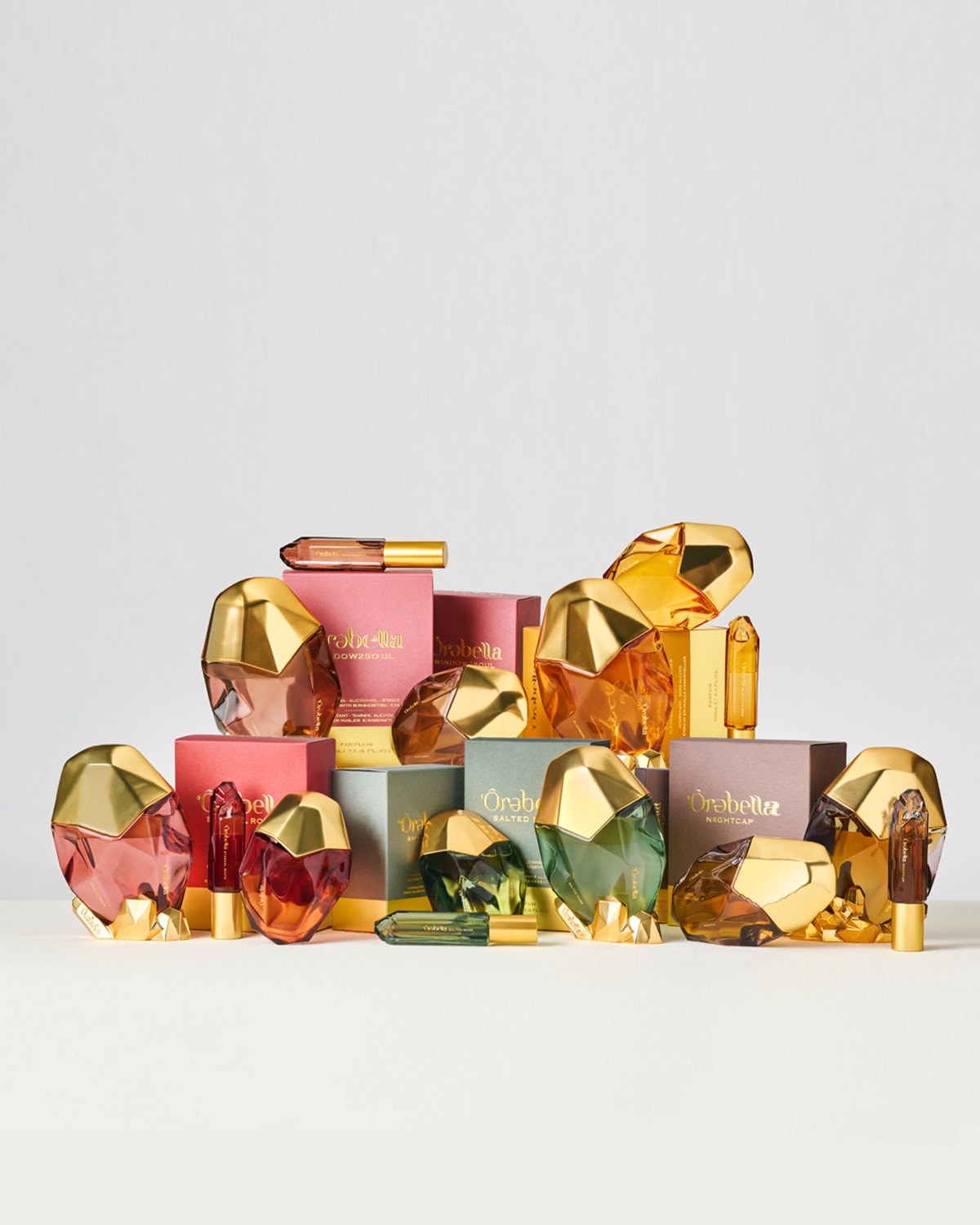 Įvairių spalvų „Ôrabela“ kvepalų kolekcija su auksiniais dangteliais ir atitinkamomis pakuotėmis, įskaitant rožinę, žalią ir gintarinę, sukuria prabangų ir kviečiantį kvapų asortimentą.