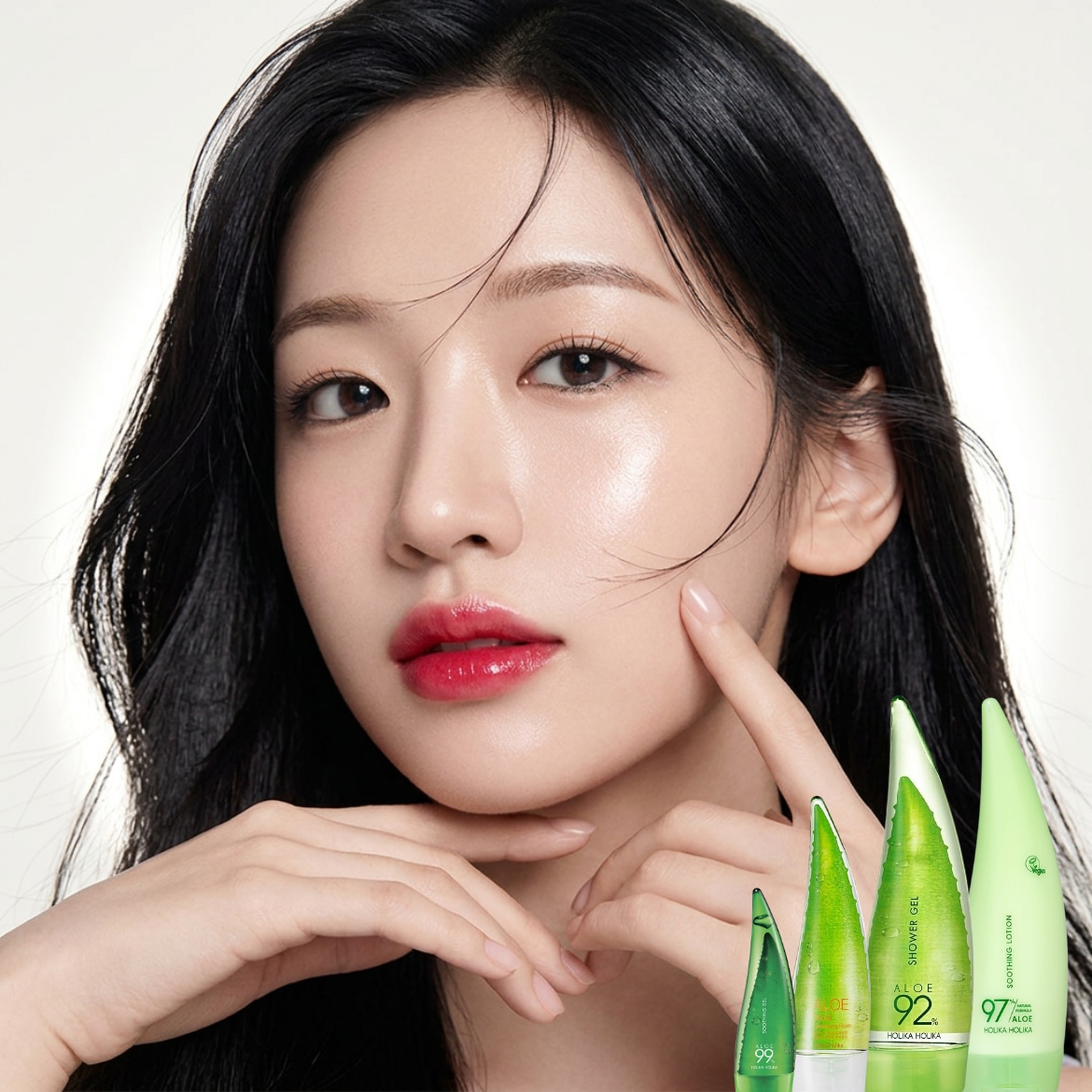 Šalia Azijos moters su raudonu lūpdažiu ir juodais plaukais matomi Holika Holika Aloe Vera produktai žaliuose buteliuose.