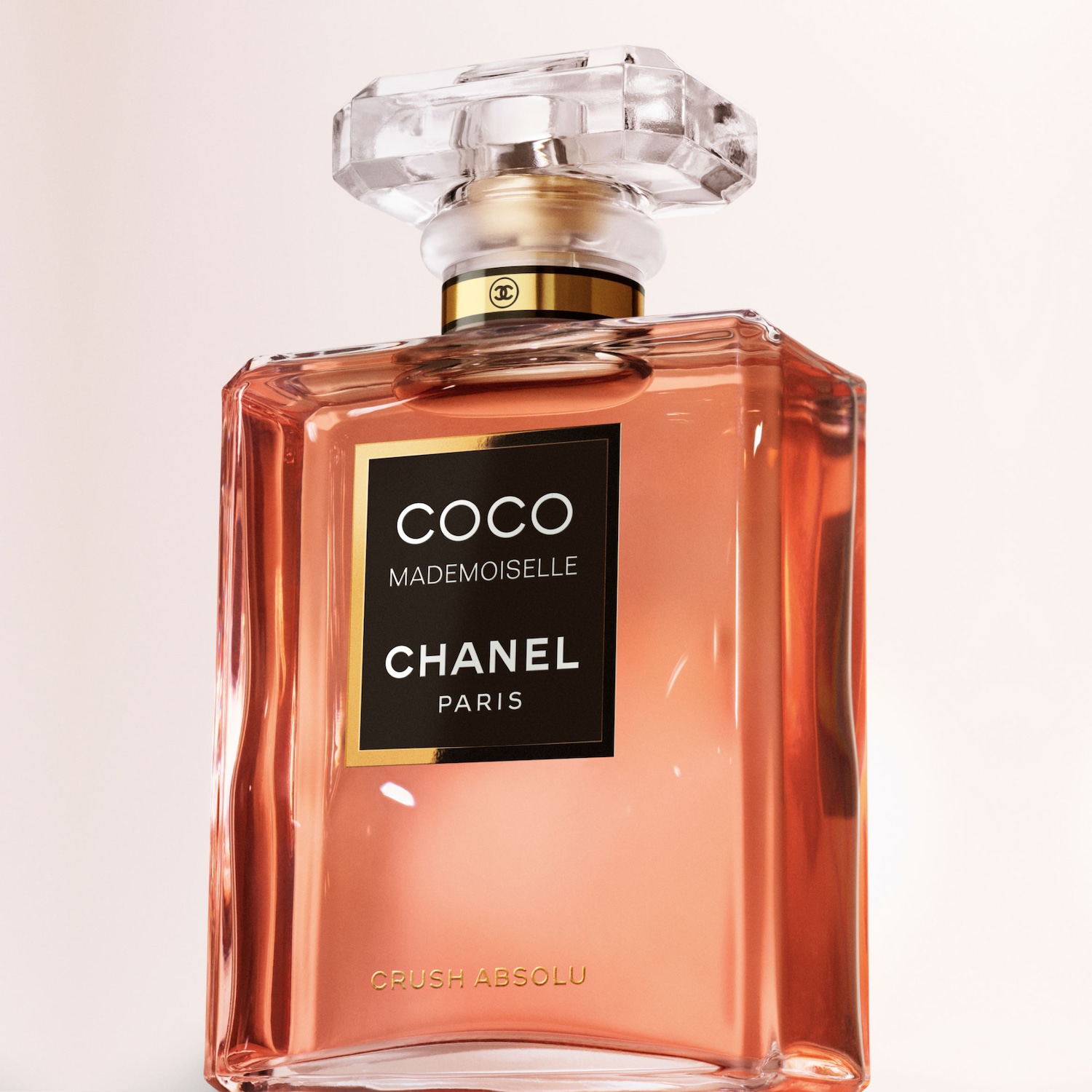 „Coco Mademoiselle Chanel Paris Crush Absolu“ kvepalų buteliukas su skaidriu dangteliu ir auksiniu kakleliu, užpildytas persikų spalvos skysčiu, yra elegantiškas ir rafinuotas.