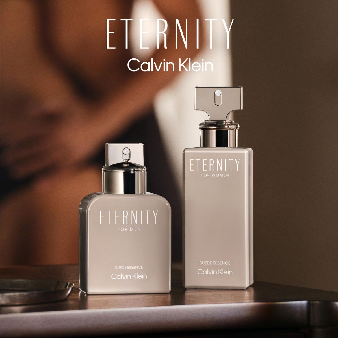„Eternity Calvin Klein“ kvepalai vyrams ir moterims, šviesiai pilkos spalvos buteliukuose su sidabriniais kamšteliais, pastatyti ant tamsaus medinio paviršiaus.