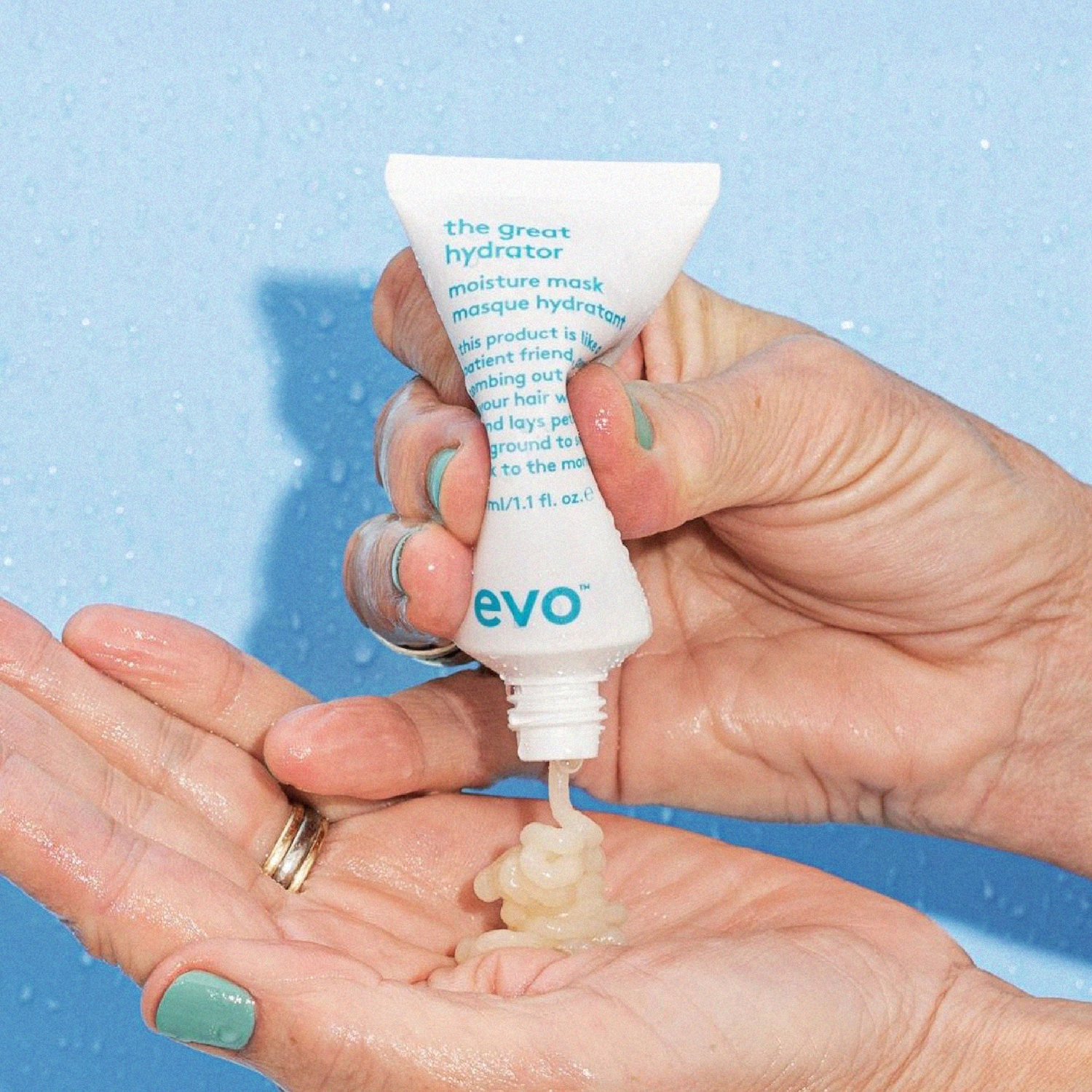 Rankos laiko baltą „Evo The Great Hydrator“ tūbelę, iš kurios į delną spaudžiamas kreminis plaukų kaukės produktas.