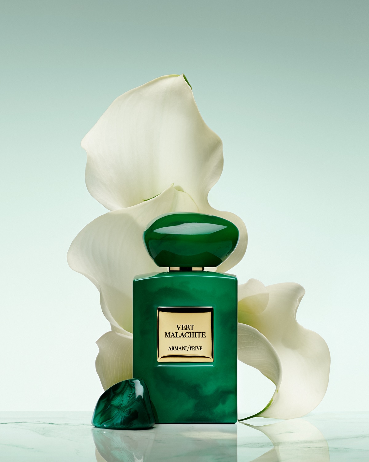 Žalias „Armani Privé Vert Malachite“ kvepalų buteliukas baltų gėlių fone.