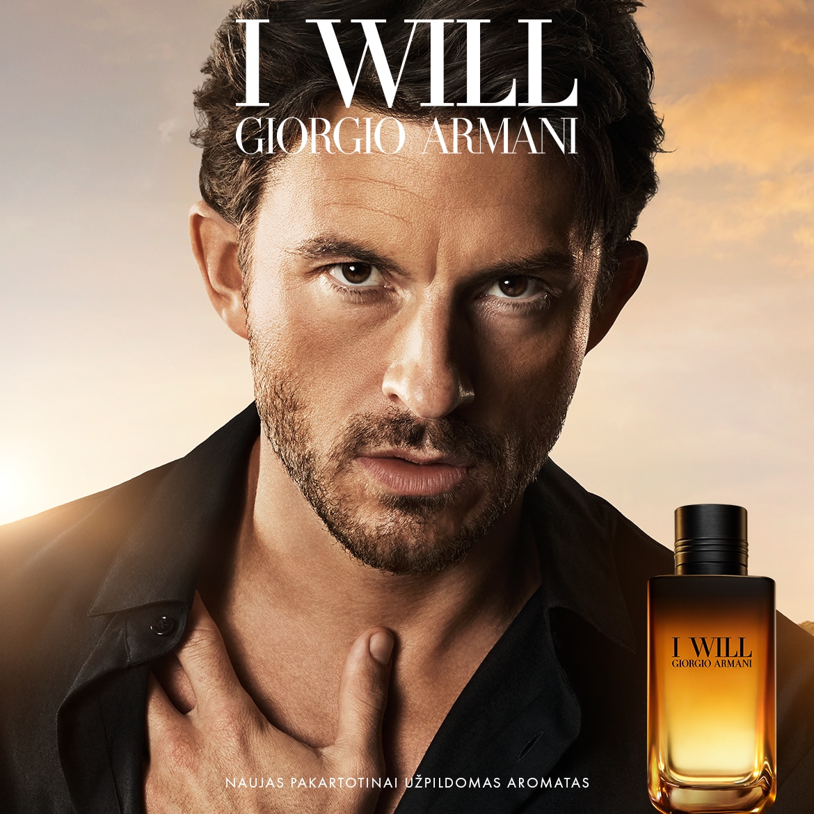 Vyras su tamsiais plaukais ir barzda, vilkintis juodus marškinius, laiko ranką ant krūtinės, o šalia jo yra „Giorgio Armani I WILL“ kvepalų buteliukas su oranžiniu ir juodu gradientu, reklamuojantis naują pakartotinai užpildomą aromatą.