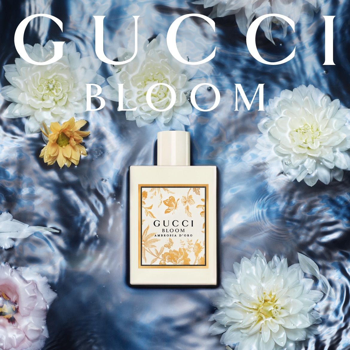 Gucci Bloom Ambrosia D'Oro aromatas baltame buteliuke su gėlėtu aukso spalvos raštu, apsuptas baltų ir geltonų žiedų ant vandens paviršiaus.