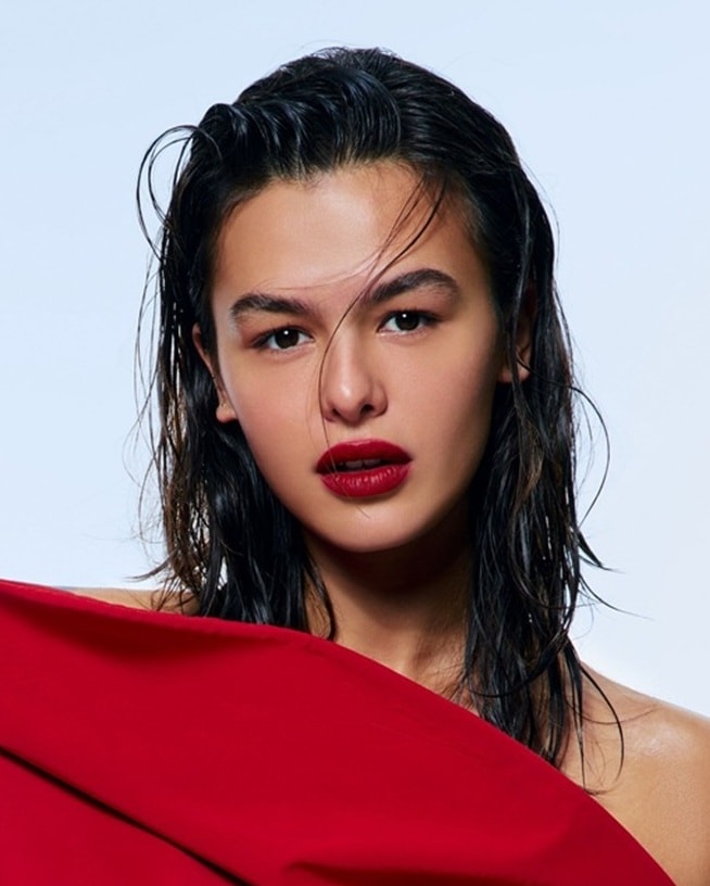 Moteris ilgais plaukais ir raudonais lūpų dažais, švelniai besišypsanti į kamerą.