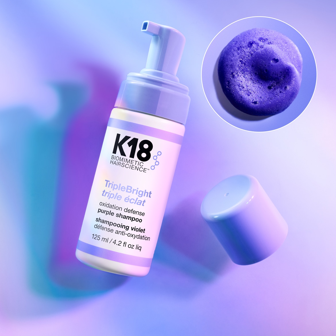 K18 Biomimetic Hairscience Triple Bright violetinis šampūnas, skirtas oksidacijos gynybai, yra 125 ml talpos buteliuke su purškikliu, o šalia matomas violetinio šampūno lašelis.