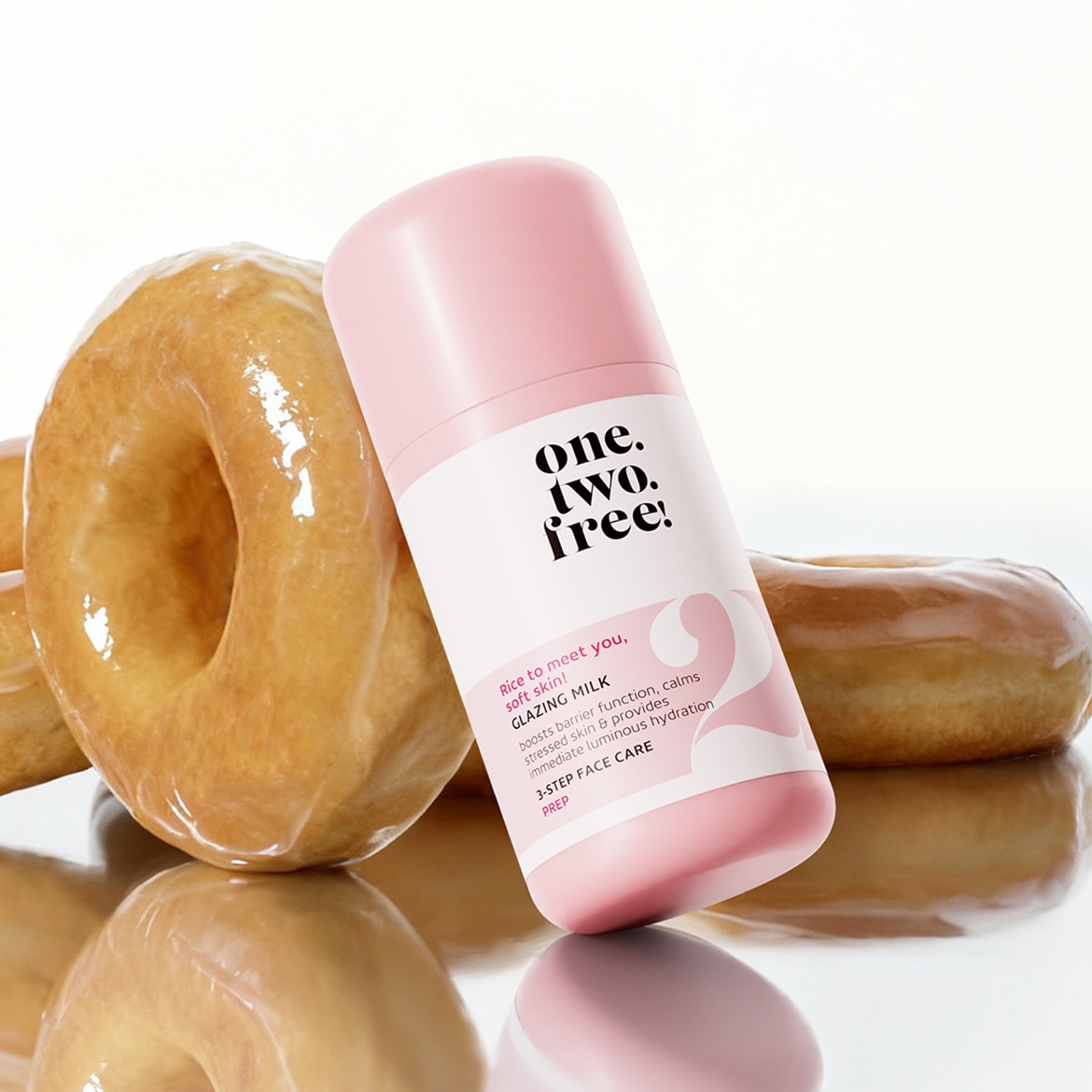 The image shows One Two Free Glazing Milk next to a glazed donut, highlighting its role in boosting skin's barrier function and providing immediate hydration for a luminous complexion.