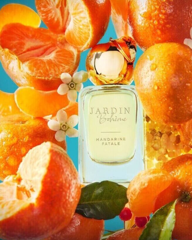 Kvepalai „Jardin Bohème Mandarine Fatale“ skaidraus stiklo buteliuke su aukso spalvos kamšteliu, apsupti mandarinų ir baltų žiedų, sukuria gaivų ir viliojantį aromatą.
