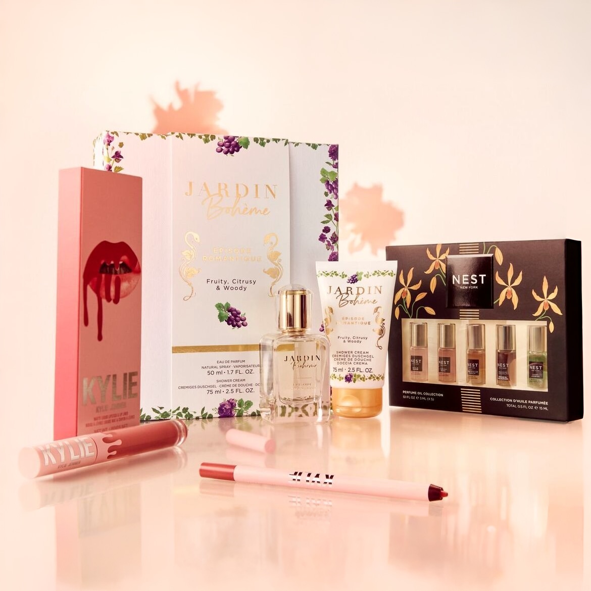 Šis paveikslėlis pristato įvairius grožio produktus, įskaitant „Kylie Cosmetics“ lūpų dažus ir pieštuką, „Jardin Bohème“ kvepalus ir dušo želė, taip pat „Nest New York“ kvepalų aliejų rinkinį.