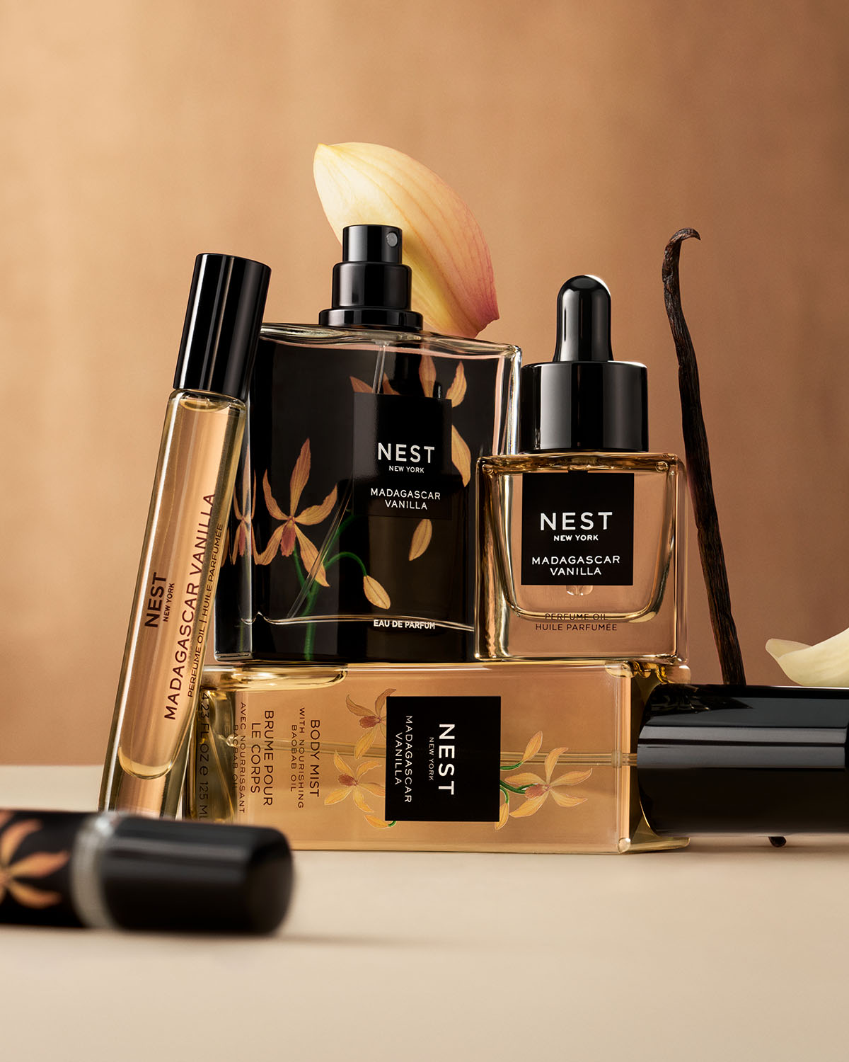 A collection of Nest New York Madagascar Vanilla products, including perfume oil, eau de parfum, and body mist, are displayed with vanilla bean and flower accents.