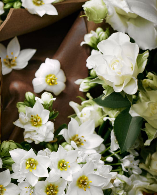 Švelnus baltų gėlių išdėstymas aplink rudos odos tekstūrą sukuria raminančią ir natūralią atmosferą