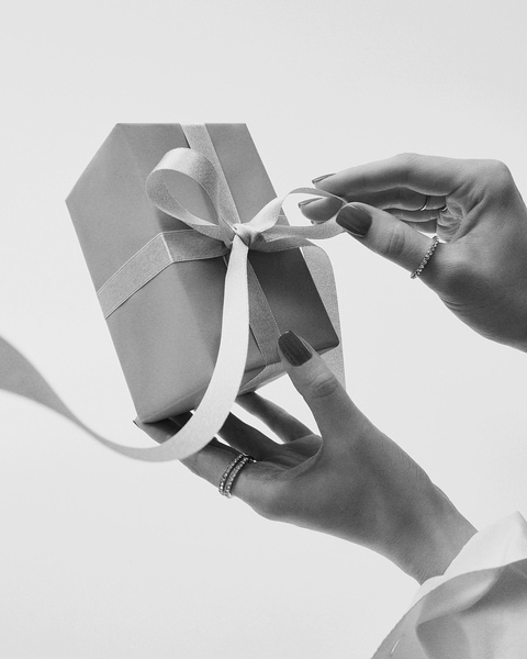 Švelniai atrišamas dovanos kaspinas, atskleidžiantis staigmeną dėžutės viduje.