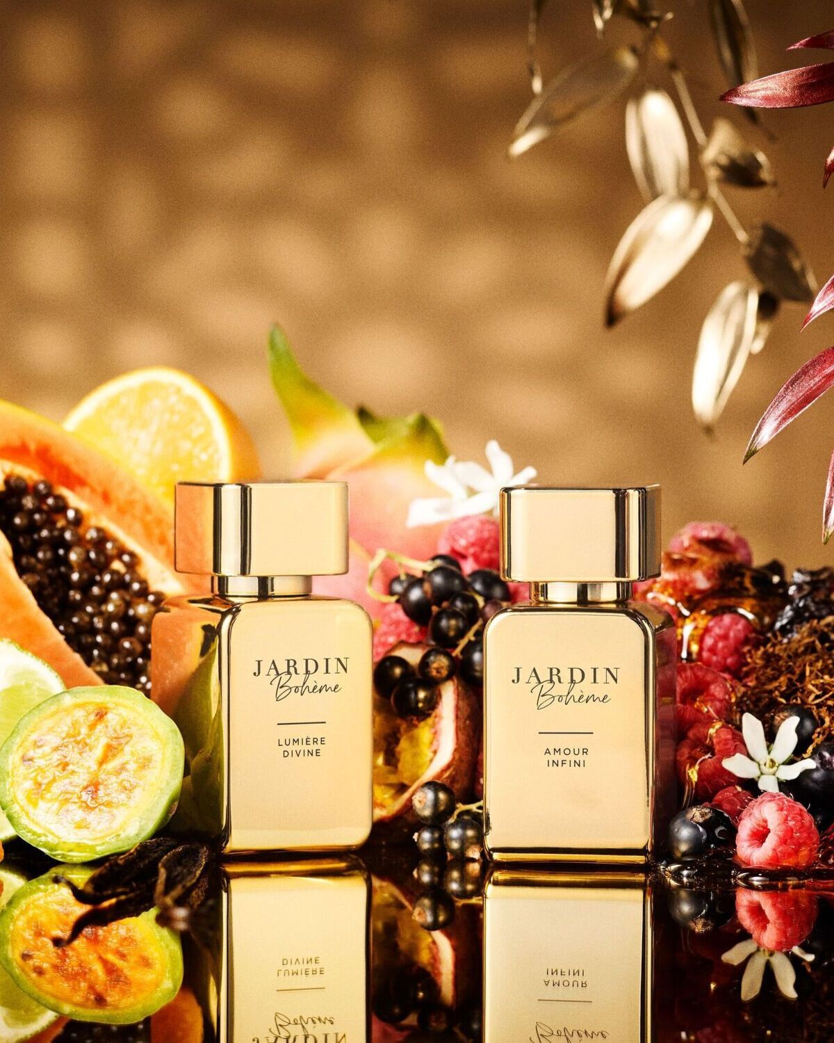 Du auksinės spalvos „Jardin Bohème“ kvepalų buteliukai, apsupti egzotiškų vaisių ir uogų, sukuria prabangos ir gamtos harmoniją.