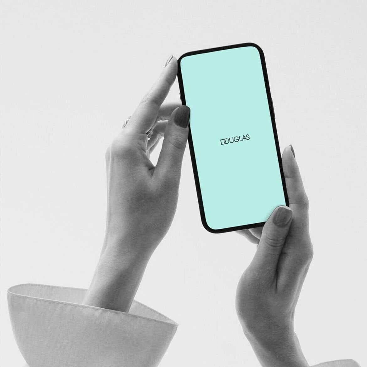 Moters rankos laiko išmanųjį telefoną su „Douglas“ logotipu ant šviesiai mėlyno ekrano.