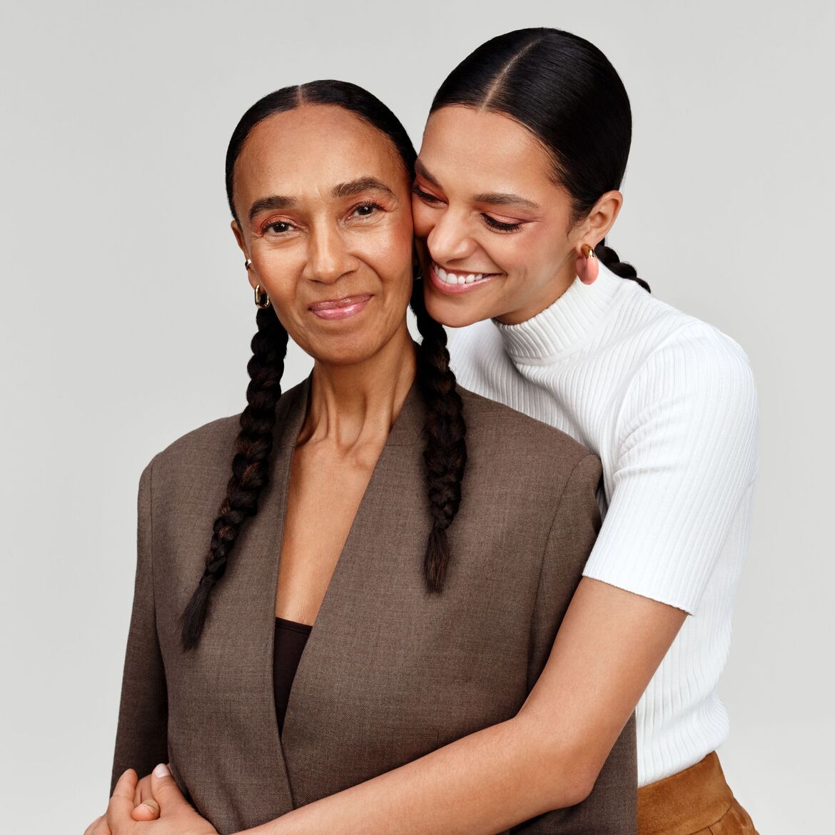 Švelnus motinos ir dukters portretas: dukra apkabina mamą, abi šypsosi, pabrėždamos artimą ryšį ir šiltą meilę.