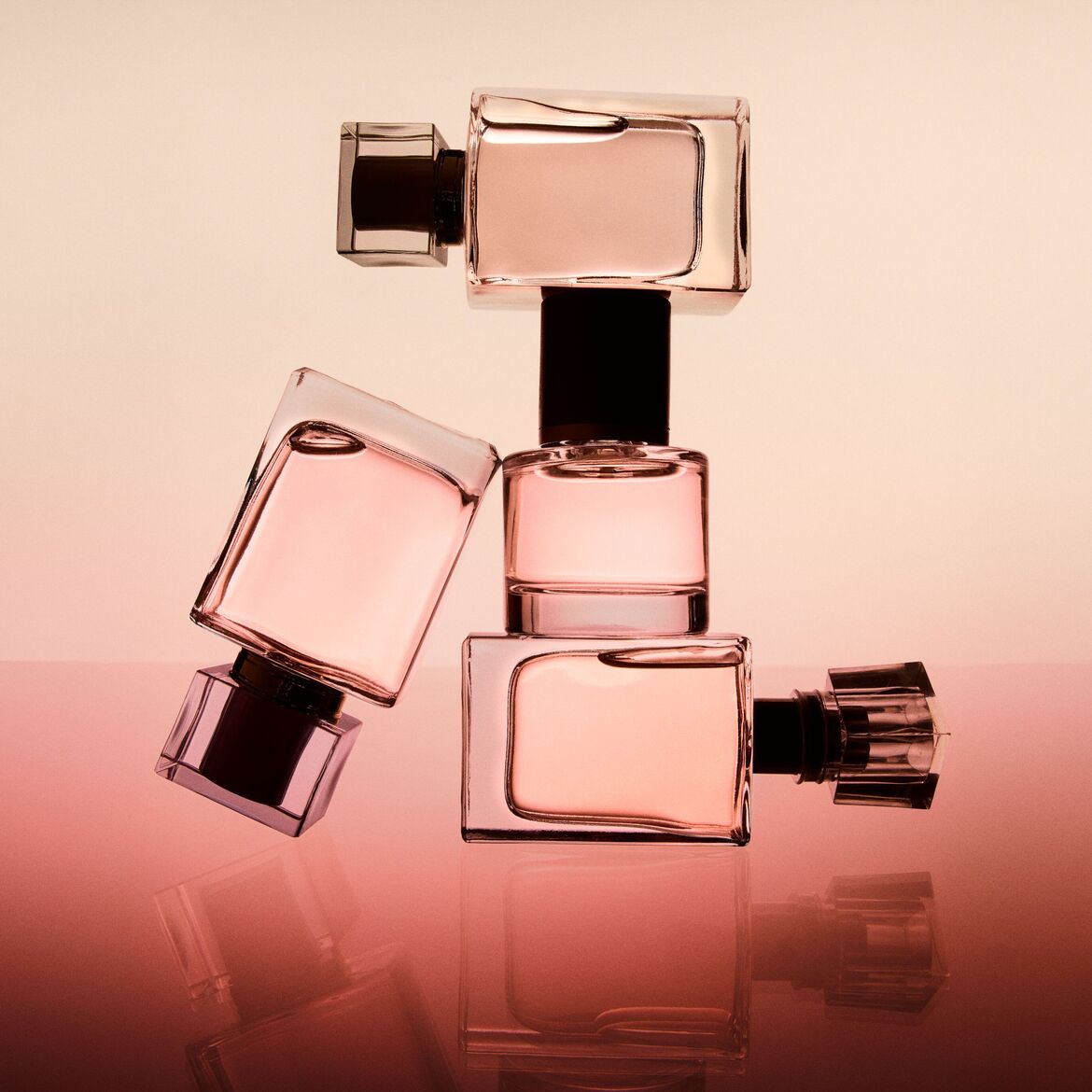 Kvepalų buteliukų kompozicija su rausvu skysčiu stikliniuose buteliukuose su juodais kamšteliais, atspindinti ant rausvo paviršiaus.