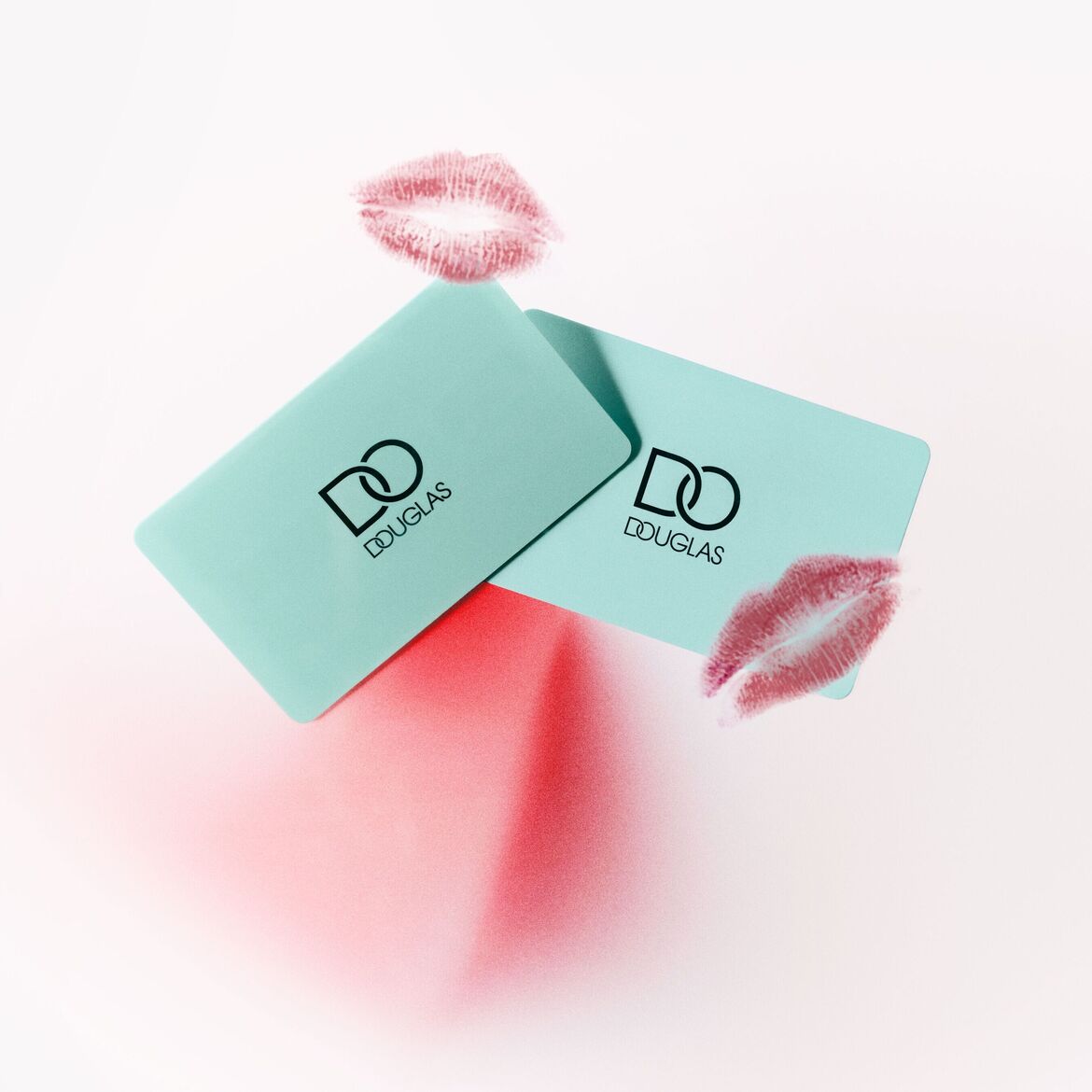 Du žalios Douglas dovanų kortelės su lūpų atspaudais ant balto paviršiaus.